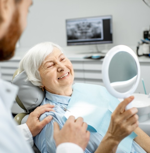 Senior woman in dental chair looking at her teeth in a mirror