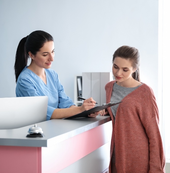 Dental team member showing a patient where to sign on a clipboard