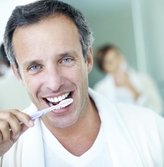 Man smiling while brushing his teeth