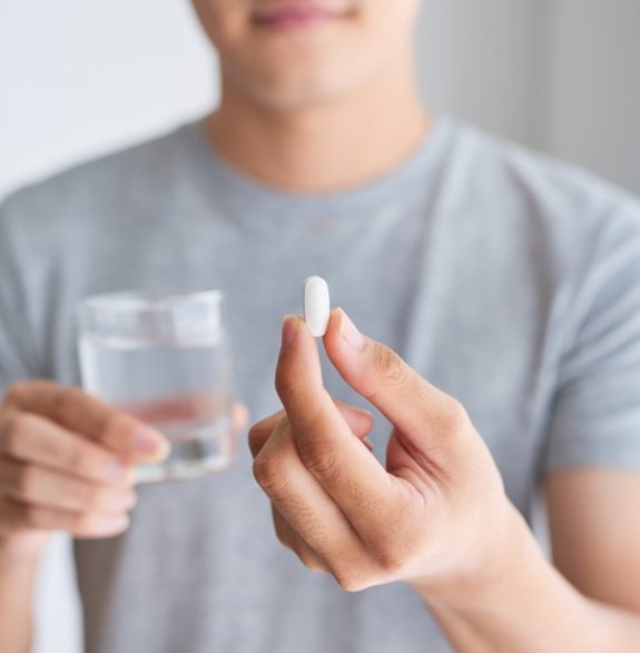 Man holding a white pill and a glass of water