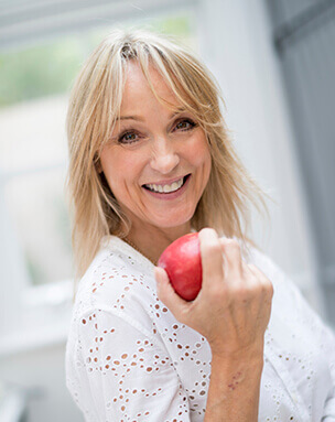 Woman wiht implant denture smiling and holding an apple